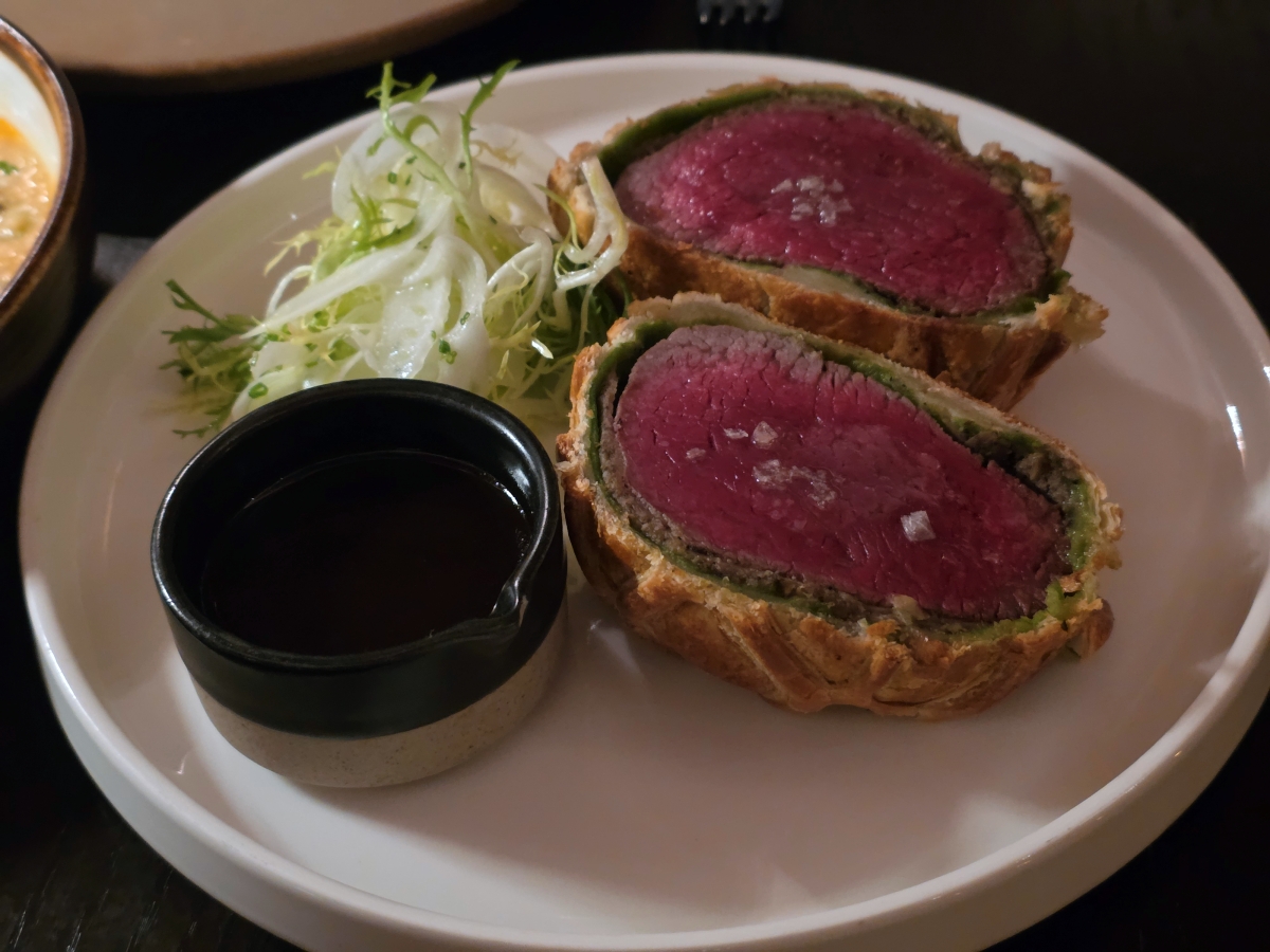 Sliced beef wellington cooked medium-rare served with a side of jus