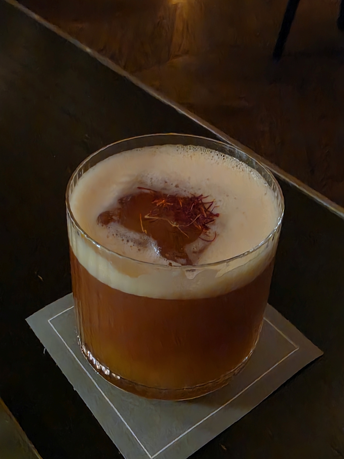 A craft cocktail with a thick foam top and garnish in a rocks glass