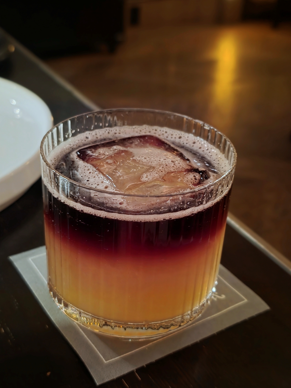 A colorful two-toned layered cocktail with a large ice cube in a rocks glass