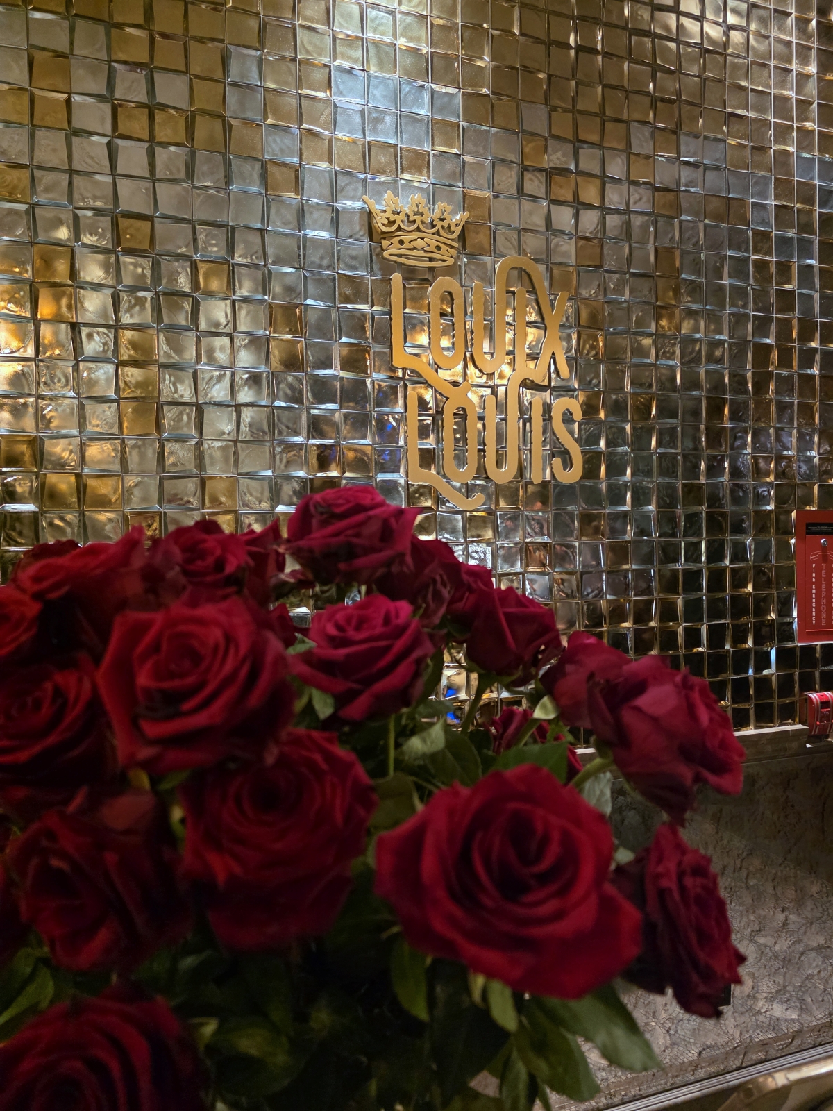 Gold Louix Louis restaurant sign surrounded by a large bouquet of red roses