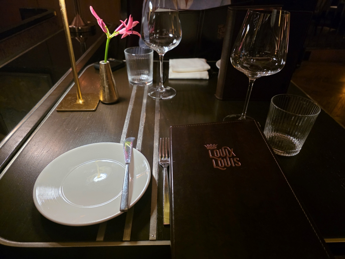Elegant restaurant table setting with Louix Louis menu, wine glasses, and a small lamp
