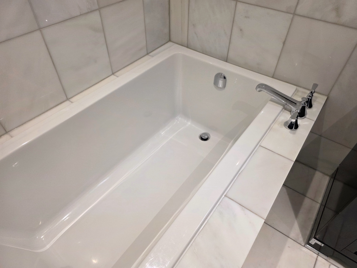 A deep white soaking bathtub surrounded by light marble in the hotel bathroom