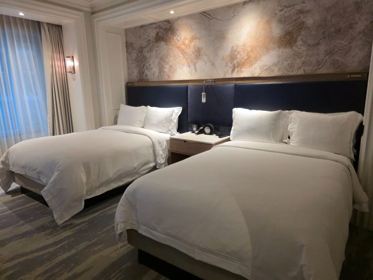 A wider angle view of the double bed guest room showing the nightstand and lighting at St.Regis Toronto