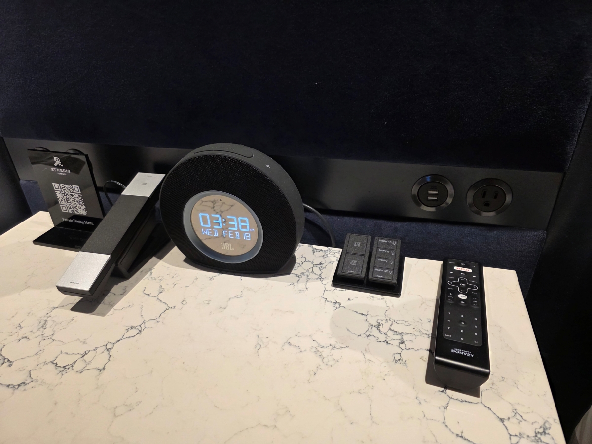 Bedside table with a modern digital alarm clock and room control remotes