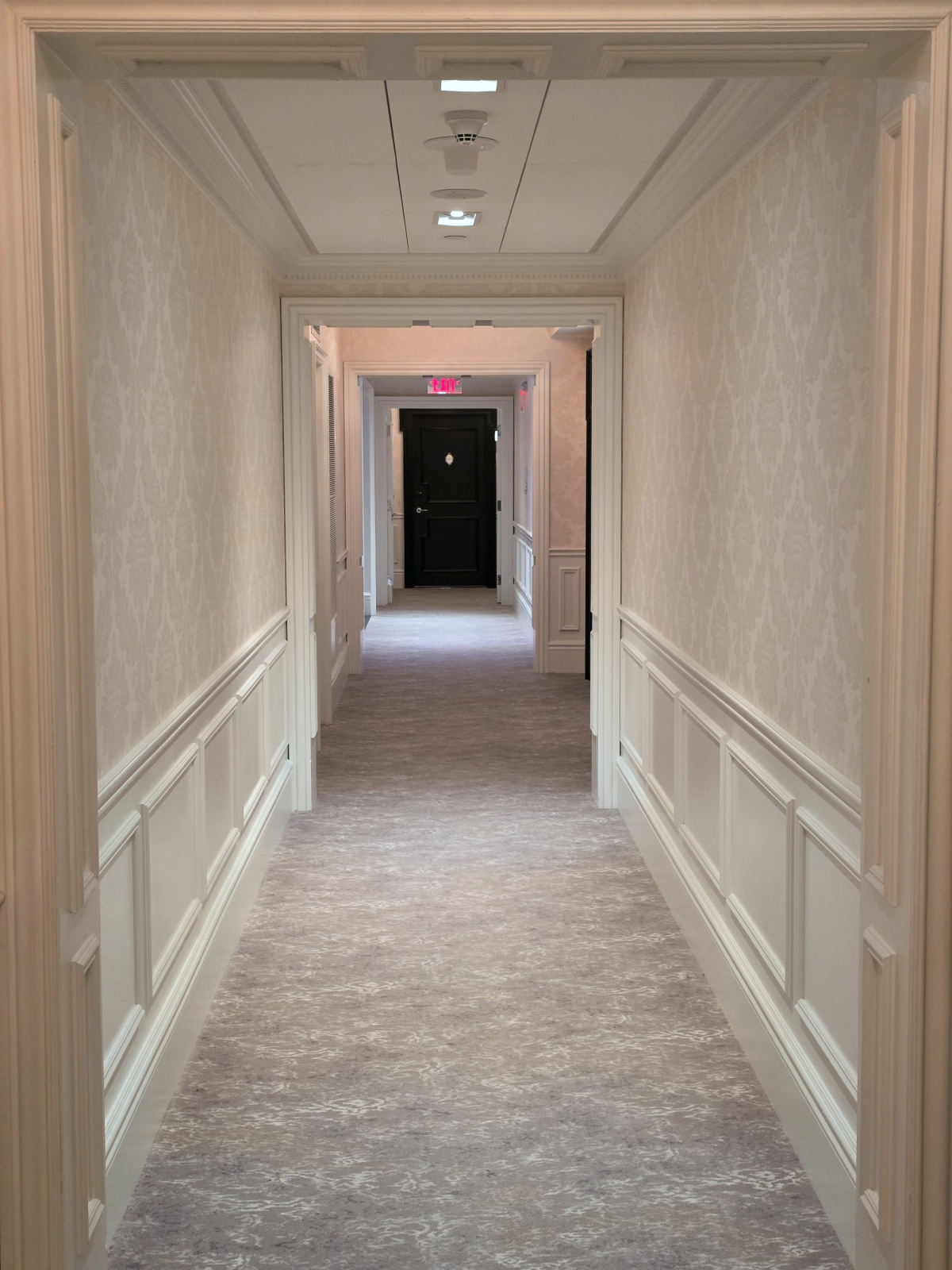 A long, brightly lit hotel hallway with patterned carpet and elegant wall moldings