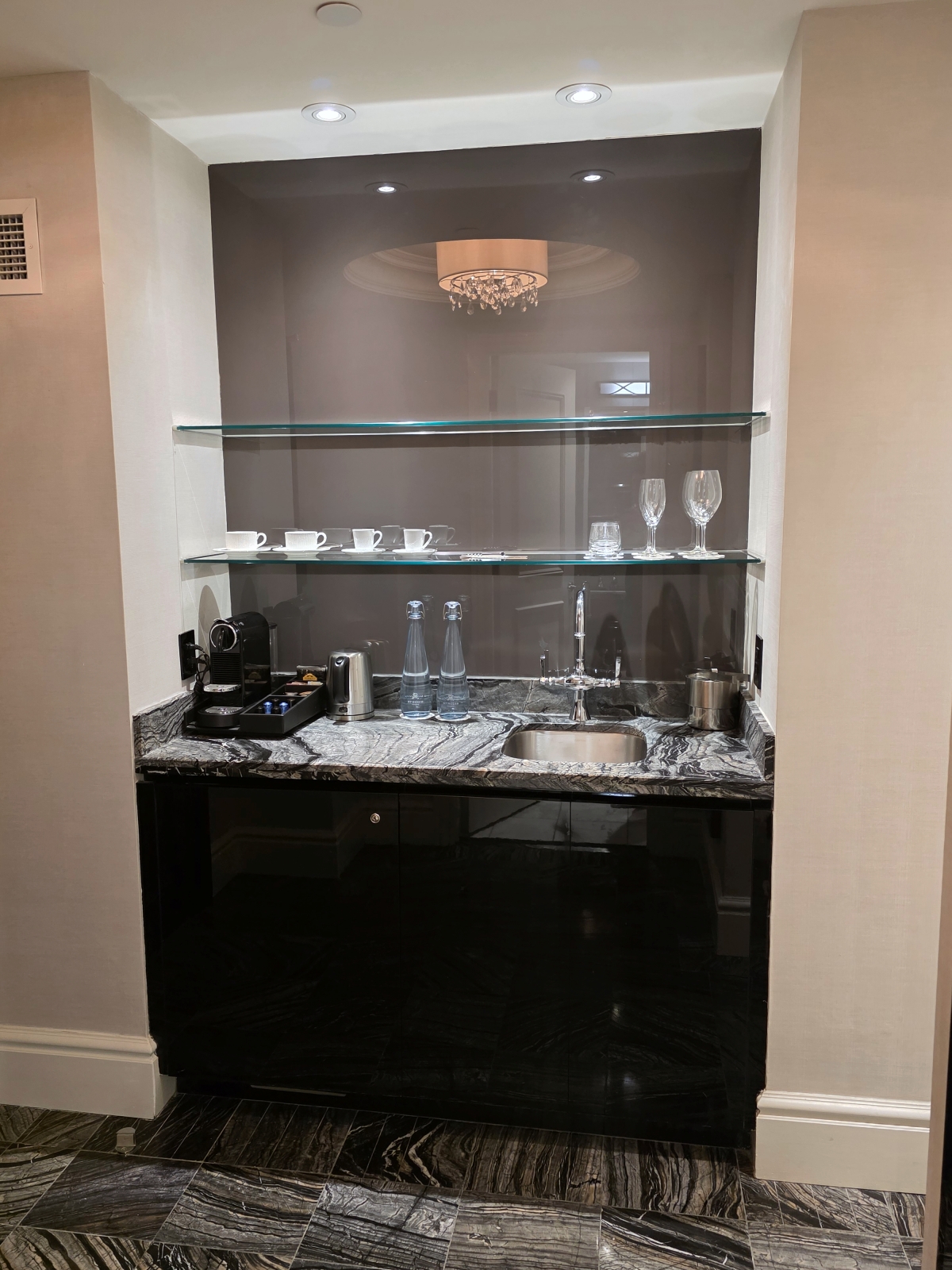 The open minibar cabinet displaying glassware, cups, and a sink area