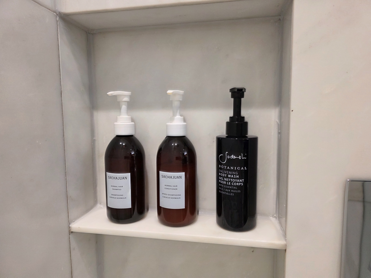 Large bottles of premium shampoo, conditioner, and body wash on a shower shelf