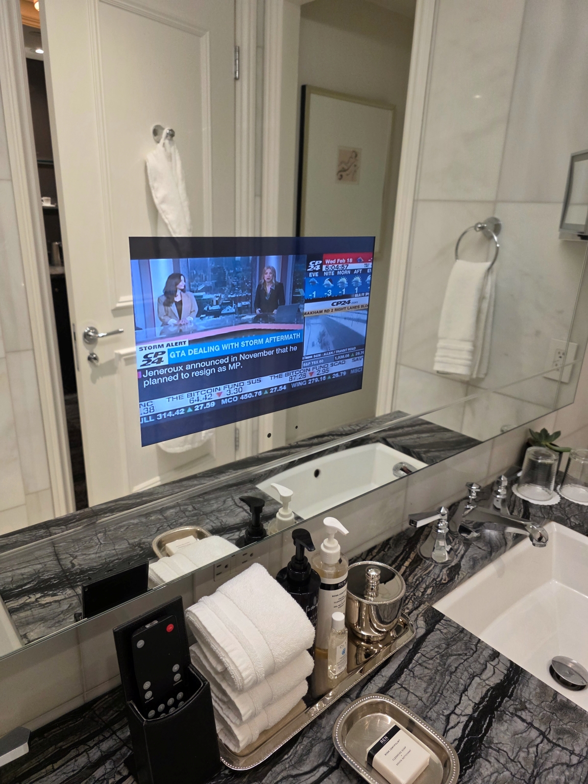 A news channel playing on a TV screen built directly into the bathroom mirror