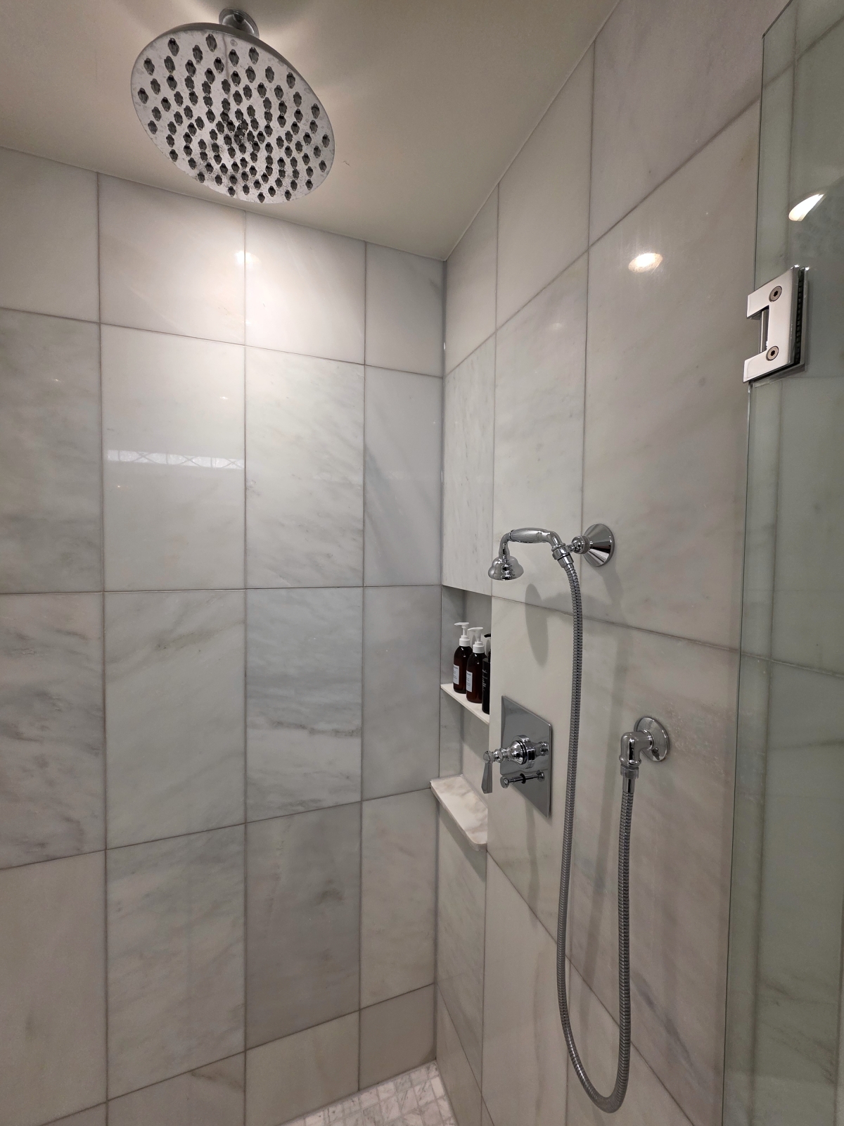 Premium chrome rainfall showerhead and handheld wand in a marble shower