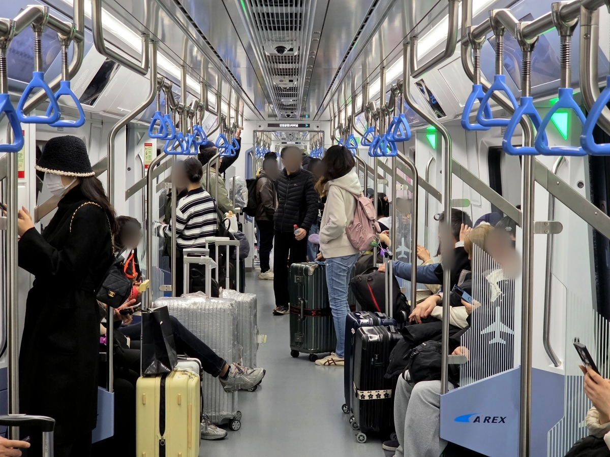 Interior of a crowded AREX All-Stop Train with passengers standing next to their suitcases